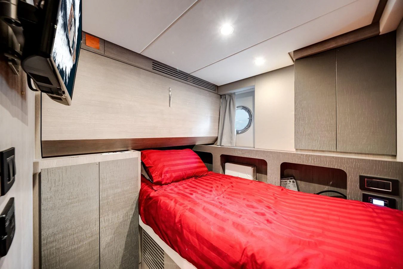 The guest cabin features a cozy single bed with vibrant red bedding and modern furnishings. aboard PARTNERSHIP V Yacht for Sale