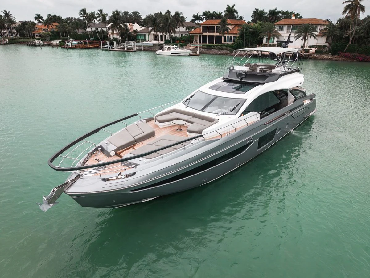 A sleek and modern yacht is anchored in a serene waterfront setting with luxurious homes in the background. aboard PARTNERSHIP V Yacht for Sale