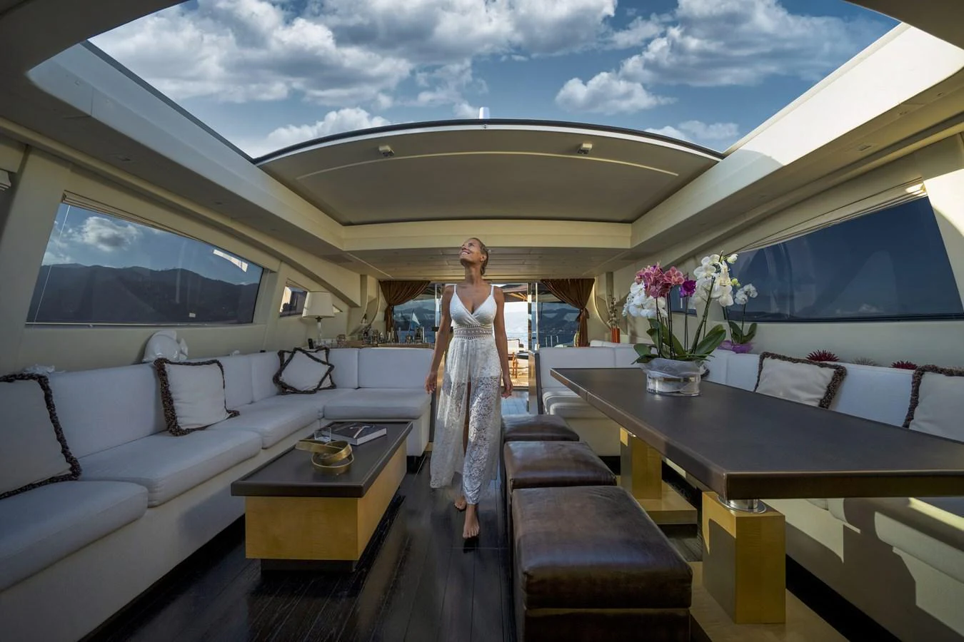 A luxurious indoor lounge area with ample seating and a stylish dining table, complemented by a large skylight and scenic views. aboard MANU Yacht for Sale