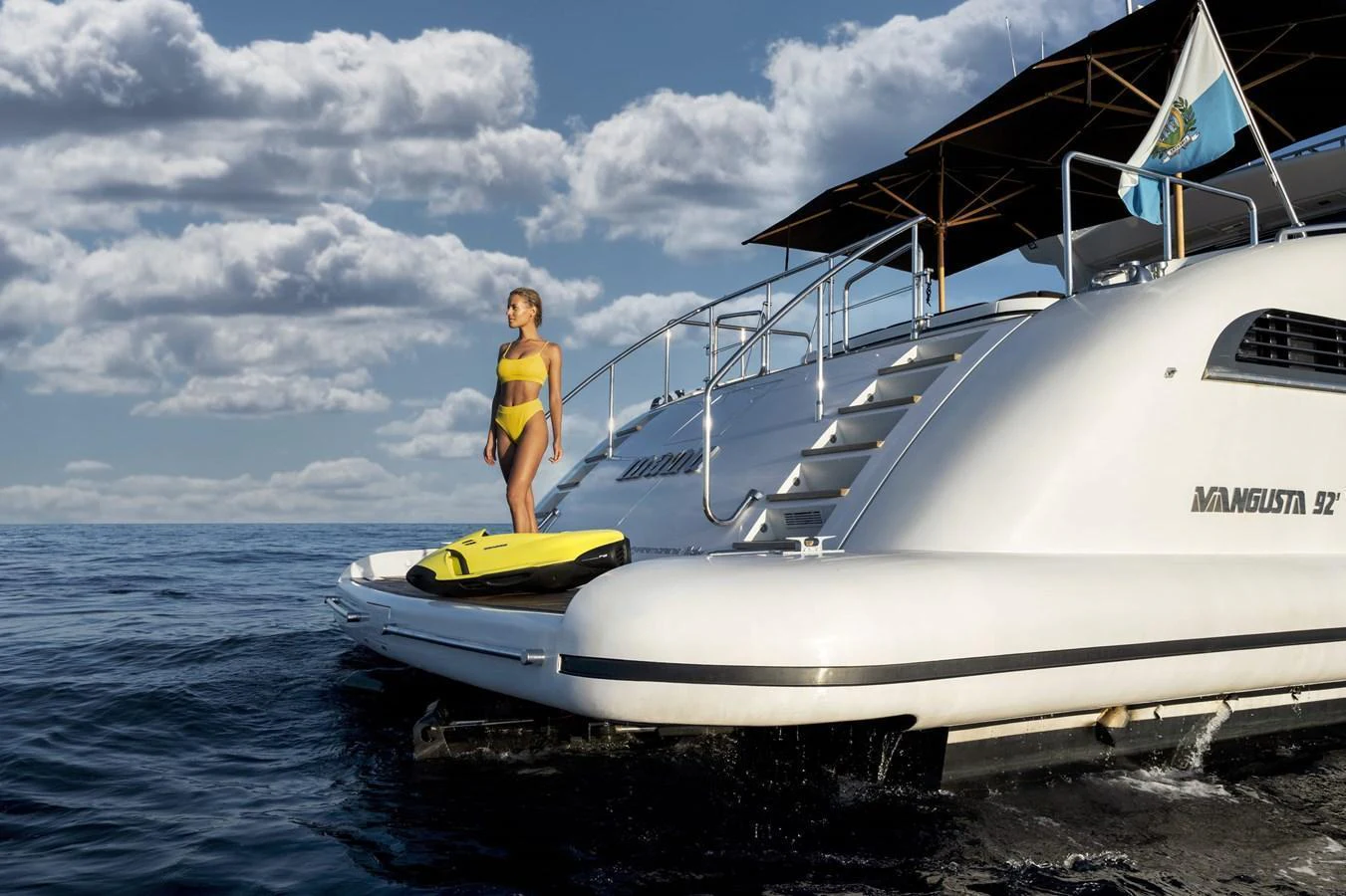A sleek yacht with a woman standing on the swim platform, enjoying the serene ocean view. aboard MANU Yacht for Sale