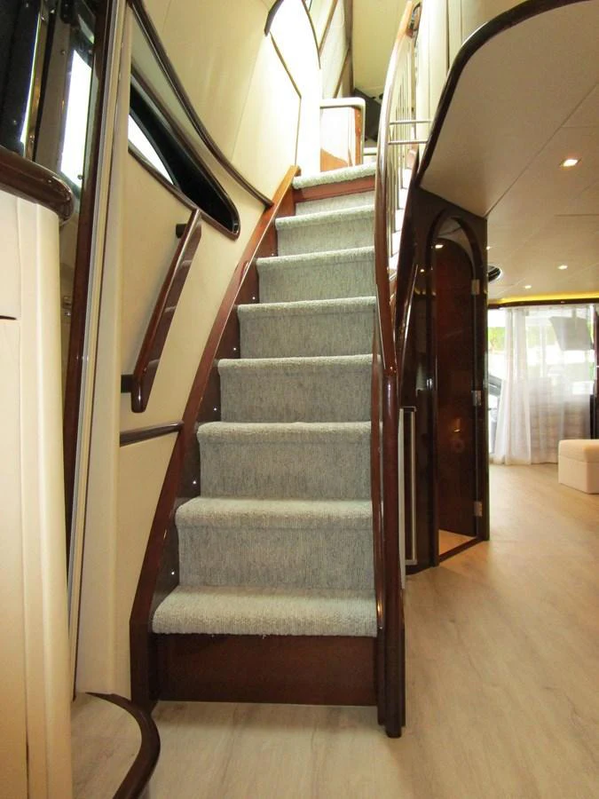 A well-lit interior staircase with wooden accents and carpeted steps leads to the upper deck. aboard SHORE GIRL Yacht for Sale