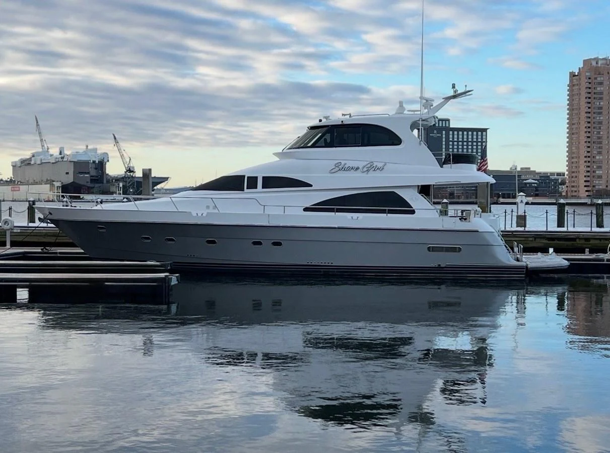 A sleek and modern yacht is docked at a marina, reflecting beautifully on the calm water. aboard SHORE GIRL Yacht for Sale