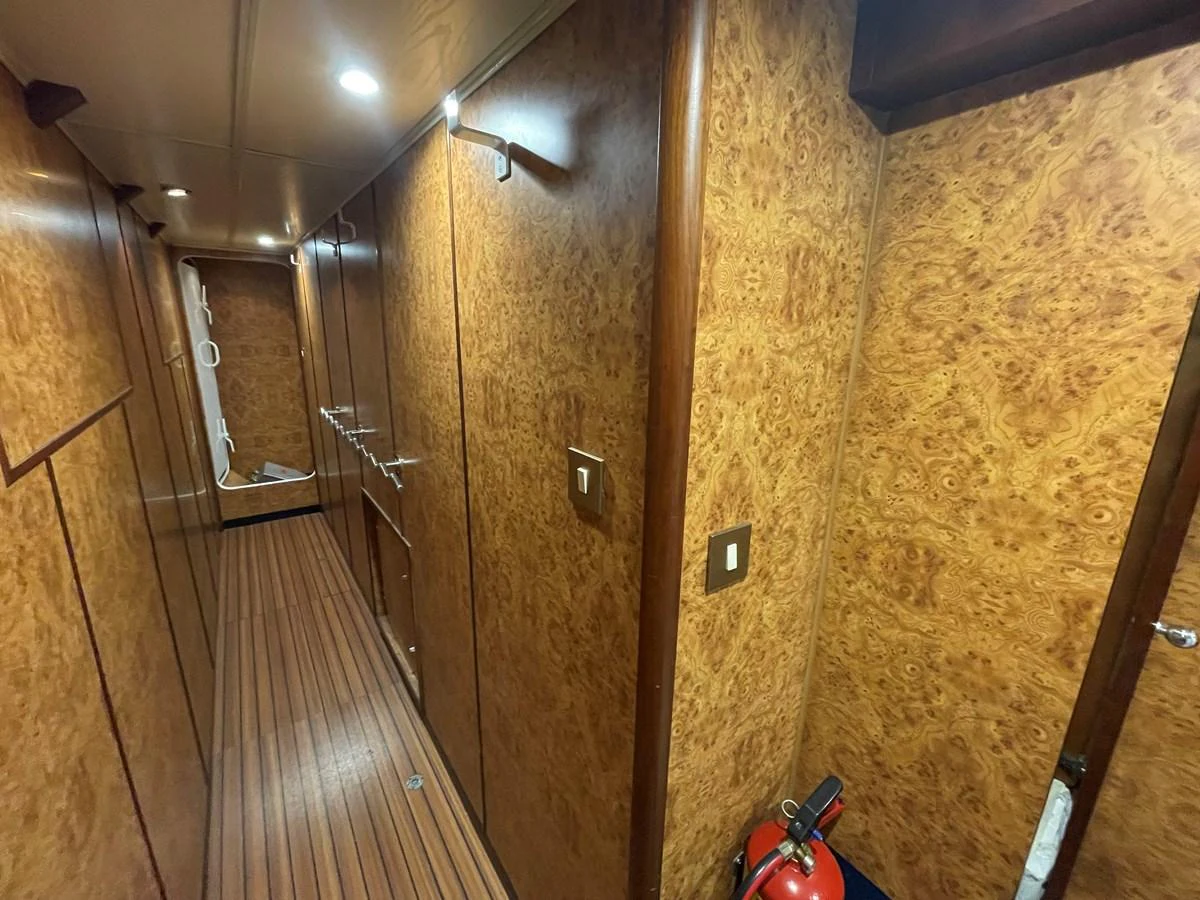 A well-appointed hallway with wooden paneling and flooring, featuring a fire extinguisher for safety. aboard ATB MAROC  CUSTOM MOTOR YACHT Yacht for Sale