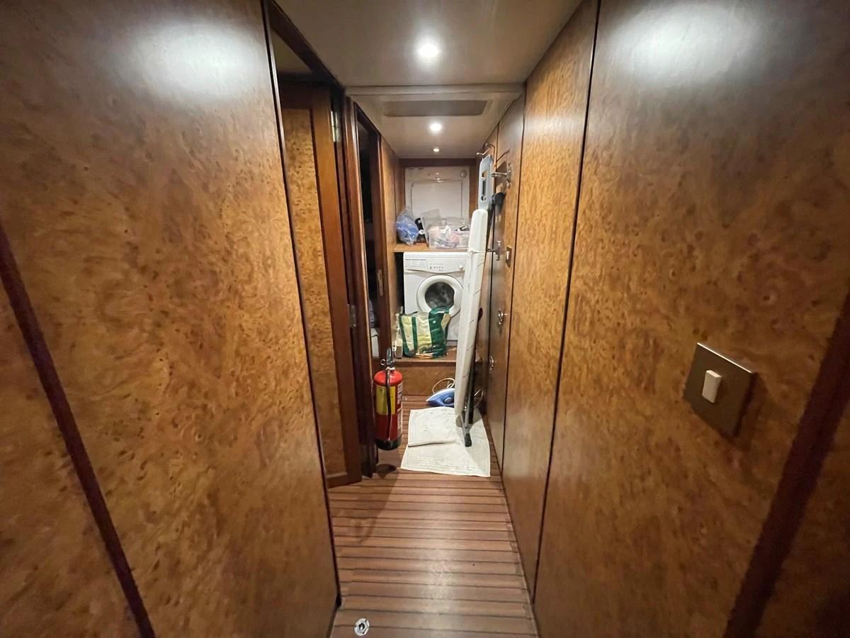 The image shows a narrow hallway leading to a laundry area with a washing machine and various items stored around. aboard ATB MAROC  CUSTOM MOTOR YACHT Yacht for Sale