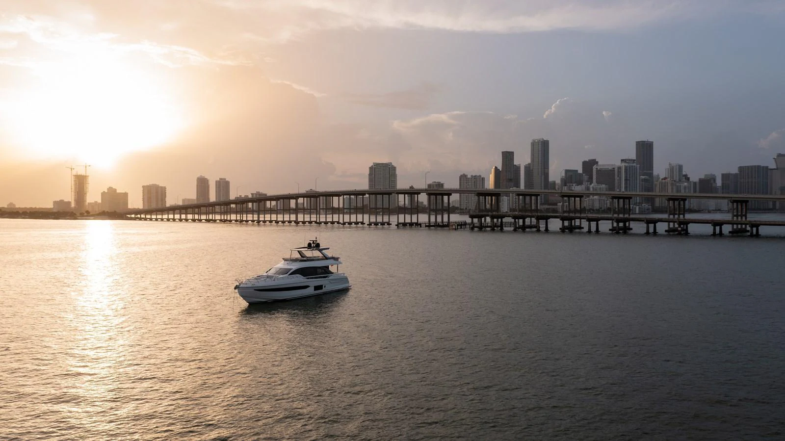 A sleek yacht cruises gracefully on calm waters with a city skyline in the background at sunset. aboard EUPHORIA Yacht for Sale