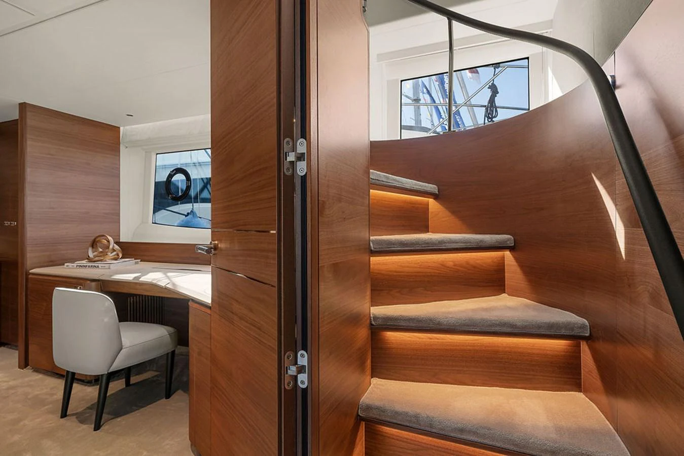 A beautifully crafted wooden staircase leads to the upper deck, complemented by a cozy workspace with a chair and desk. aboard PRINCESS S72 Yacht for Sale