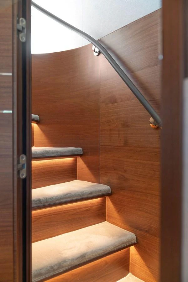 A sleek wooden staircase with soft lighting leads to the upper deck. aboard PRINCESS S72 Yacht for Sale