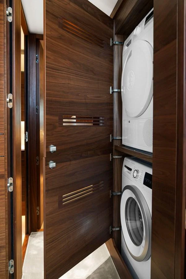 This image showcases a neatly integrated laundry area with a washer and dryer behind wooden cabinetry. aboard PRINCESS S72 Yacht for Sale