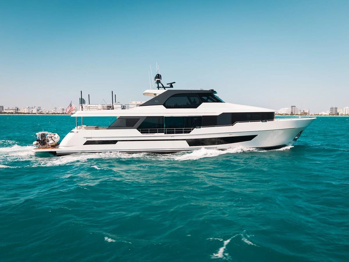 A sleek and modern yacht cruises through clear blue waters with a cityscape in the background. aboard LA LA LA Yacht for Sale