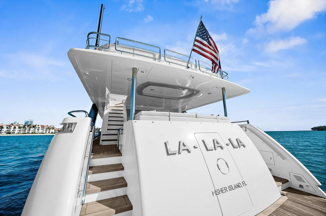 The yacht's aft deck features a spacious and inviting area with a grand staircase leading to the upper deck, complemented by a prominent American flag. aboard LA LA LA Yacht for Sale