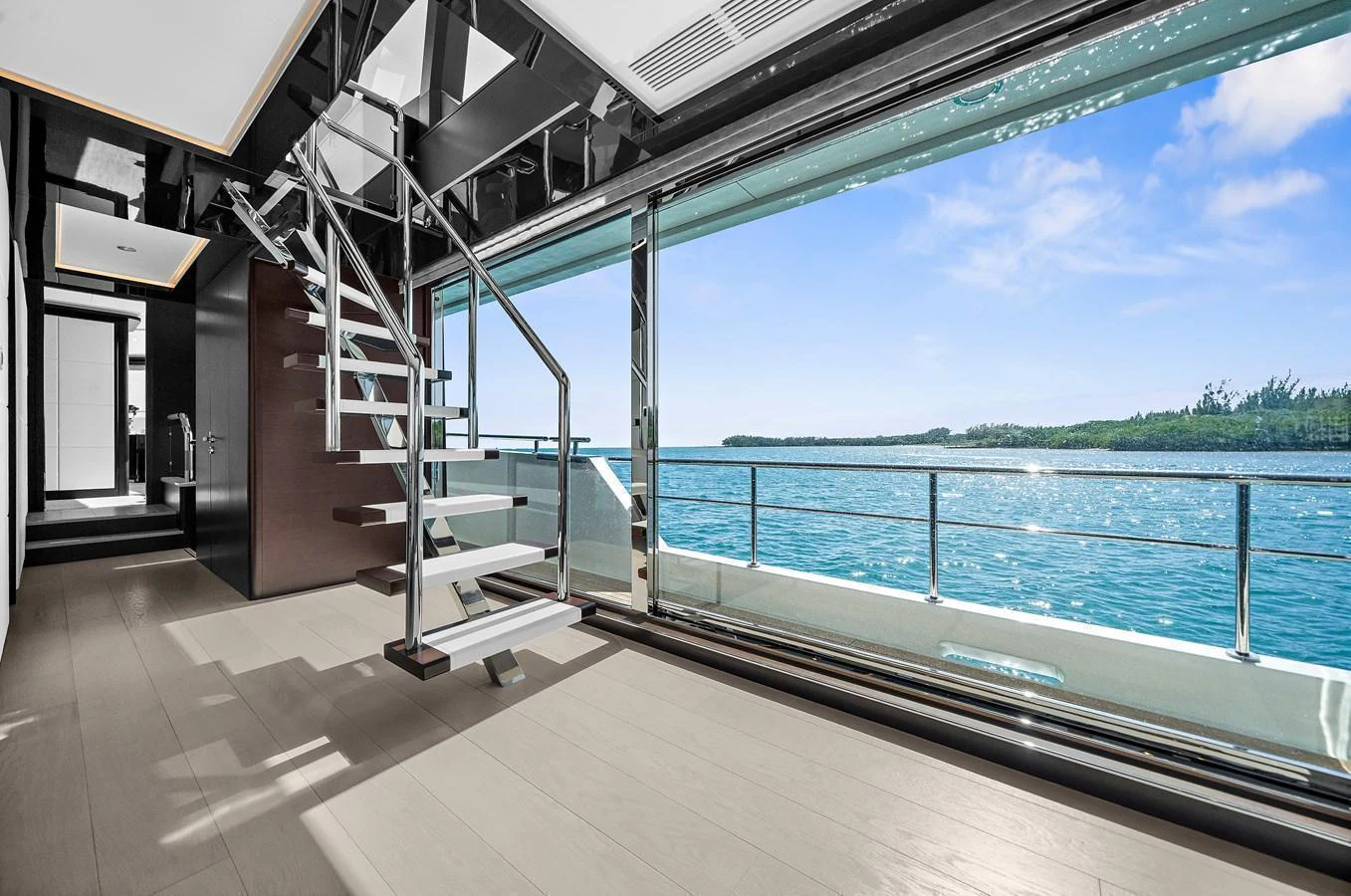 A modern yacht interior with a sleek staircase and expansive ocean views through large windows. aboard LA LA LA Yacht for Sale