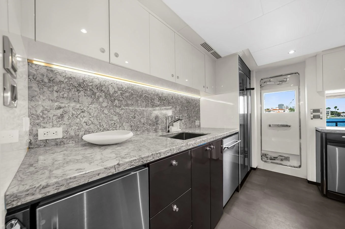 The galley features modern appliances and sleek countertops with a view of the water through the door. aboard LA LA LA Yacht for Sale