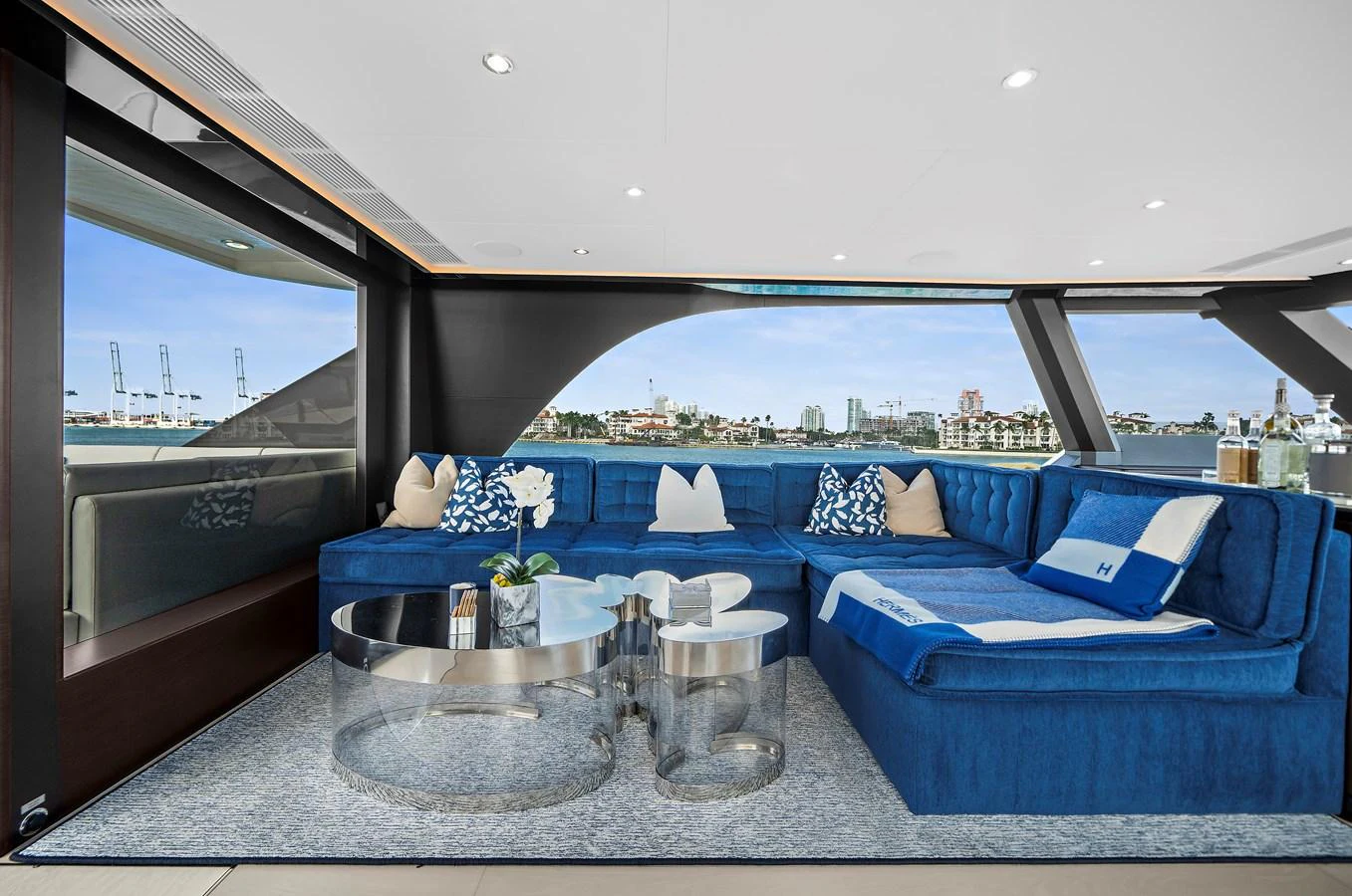 The salon features a luxurious seating area with plush blue sofas and panoramic windows offering stunning views. aboard LA LA LA Yacht for Sale