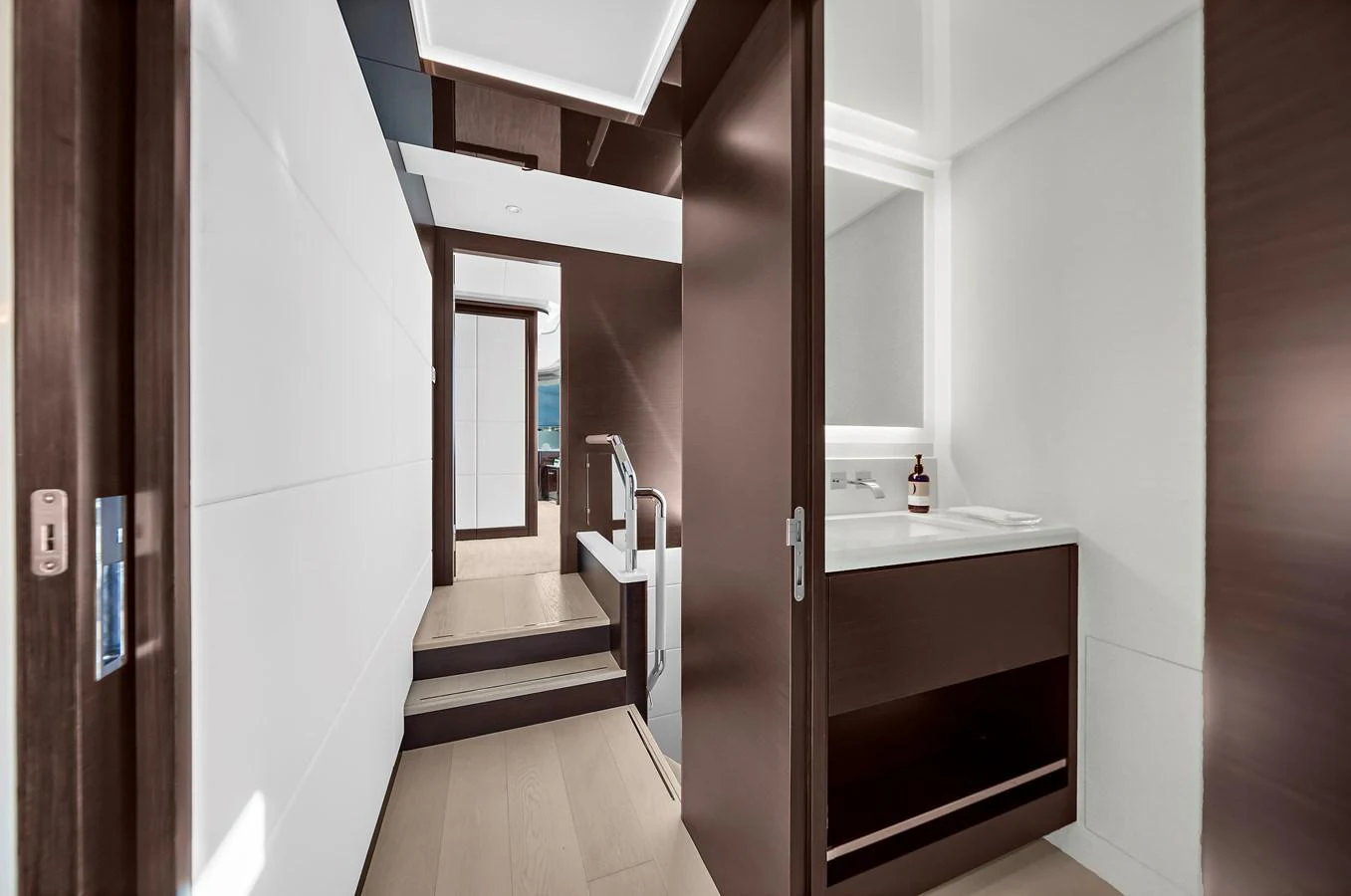 A modern yacht interior featuring a sleek hallway with a staircase and a bathroom. aboard LA LA LA Yacht for Sale