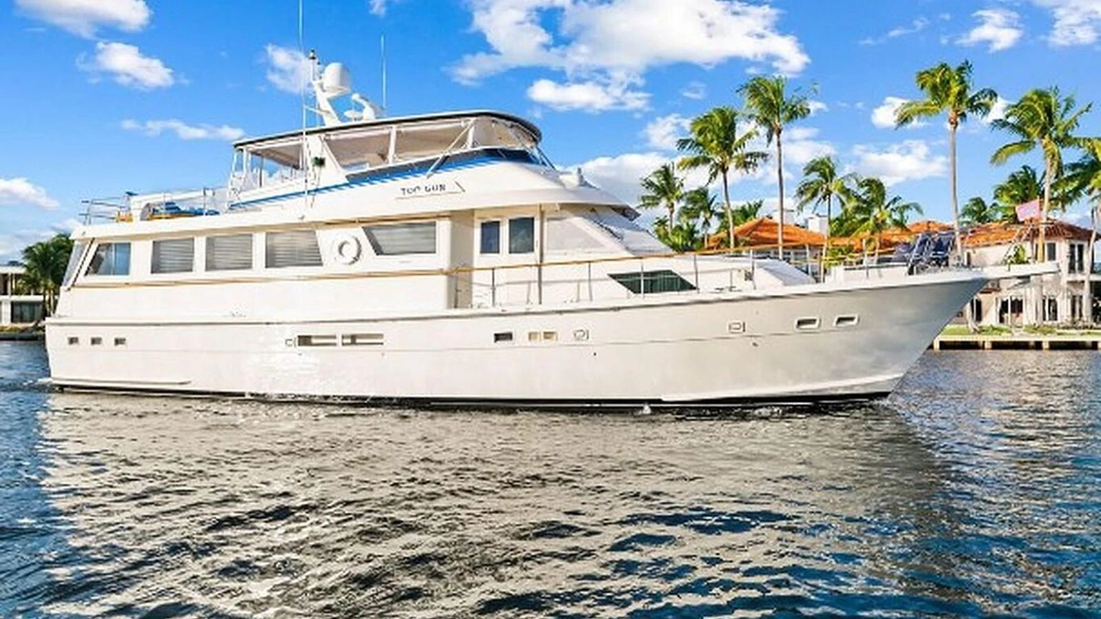 A luxurious yacht cruises along a serene waterfront with palm trees in the background. aboard TOP GUN Yacht for Sale