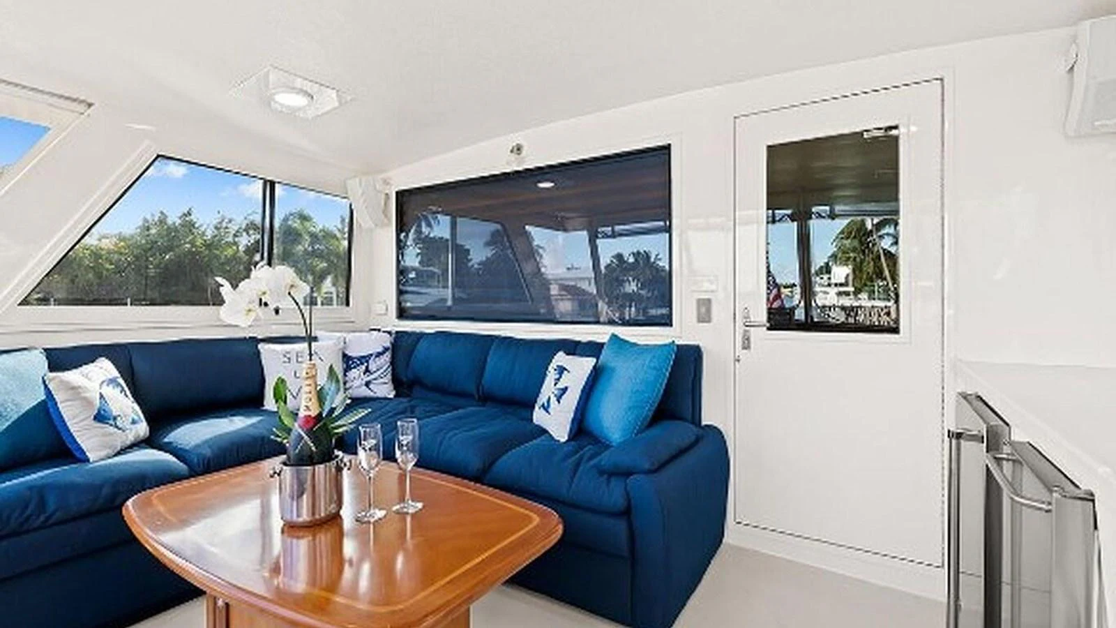 The salon features a comfortable seating area with a plush blue sofa and a wooden coffee table, complemented by natural light from large windows. aboard TOP GUN Yacht for Sale
