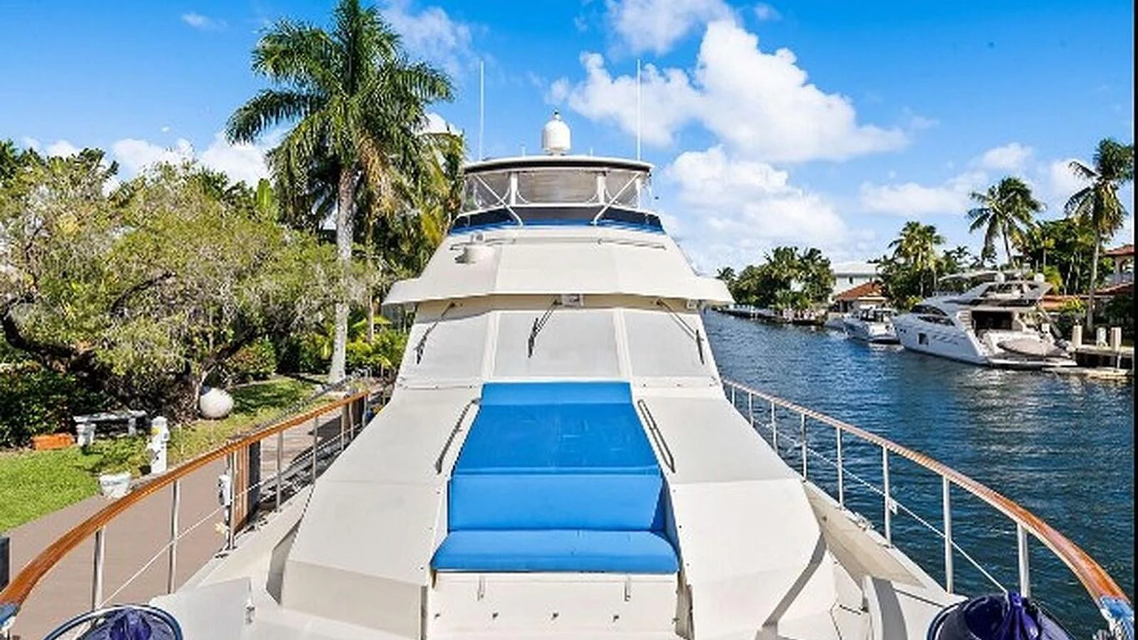 The yacht's foredeck features a spacious sunbathing area with a blue cushion, set against a scenic waterfront backdrop. aboard TOP GUN Yacht for Sale