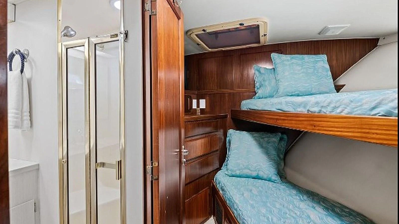 A cozy cabin with bunk beds and an adjacent bathroom, featuring wood paneling and soft bedding. aboard TOP GUN Yacht for Sale