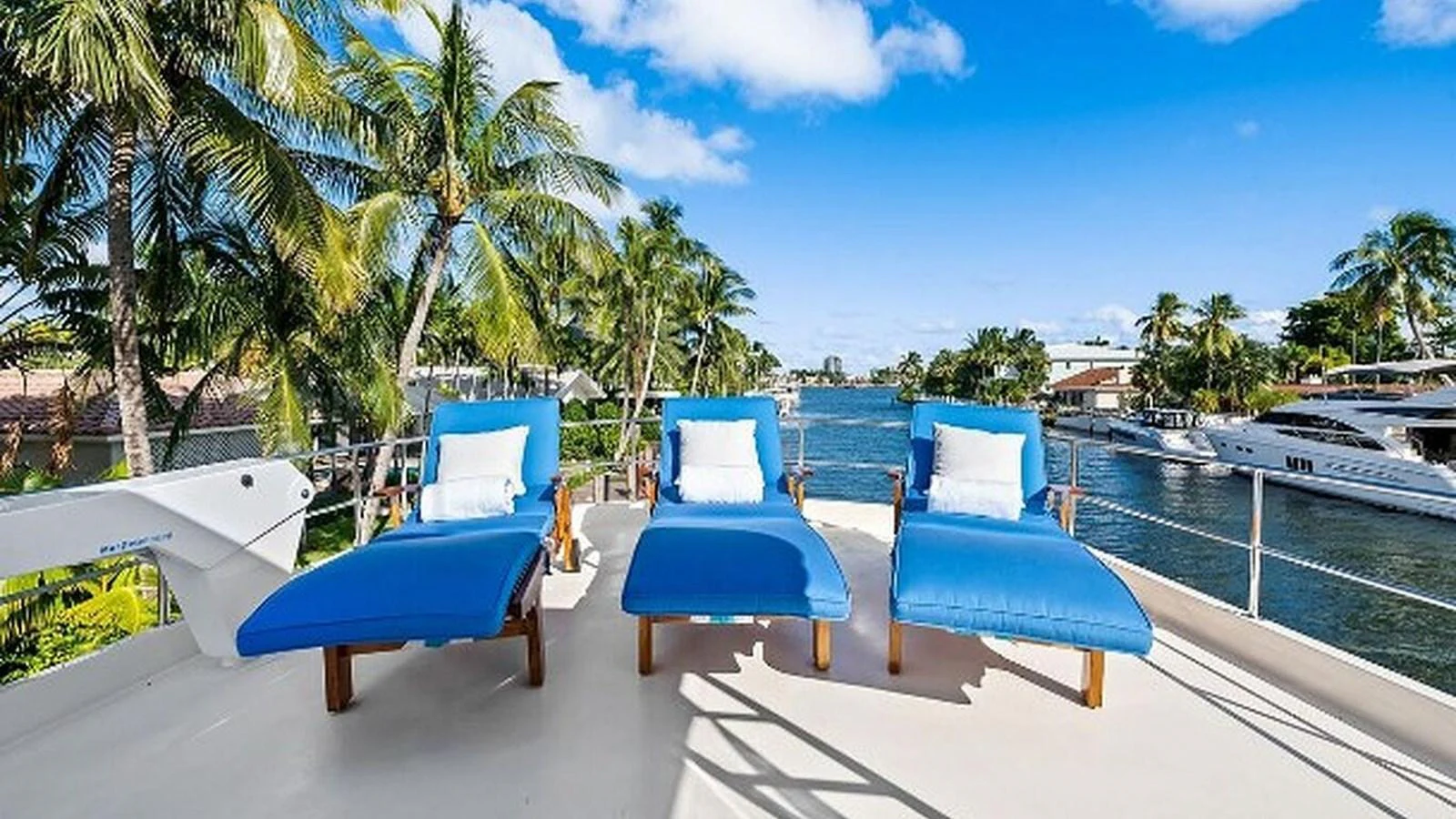 The sundeck features comfortable blue loungers with a scenic view of the waterway and palm trees. aboard TOP GUN Yacht for Sale