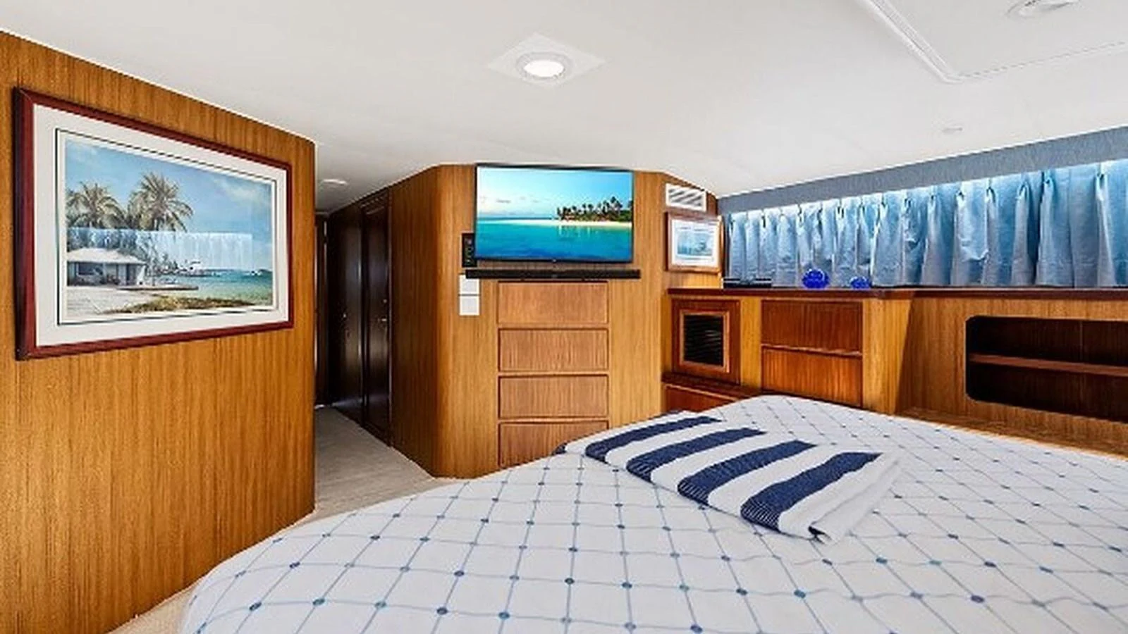 The stateroom features a comfortable bed with a striped towel, wooden cabinetry, and a mounted TV for a cozy retreat. aboard TOP GUN Yacht for Sale
