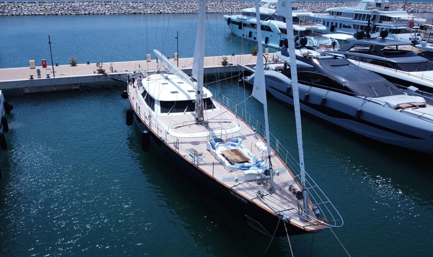A sleek sailing yacht is docked in a marina, showcasing its elegant design and spacious deck. aboard HERITAGE M Yacht for Sale