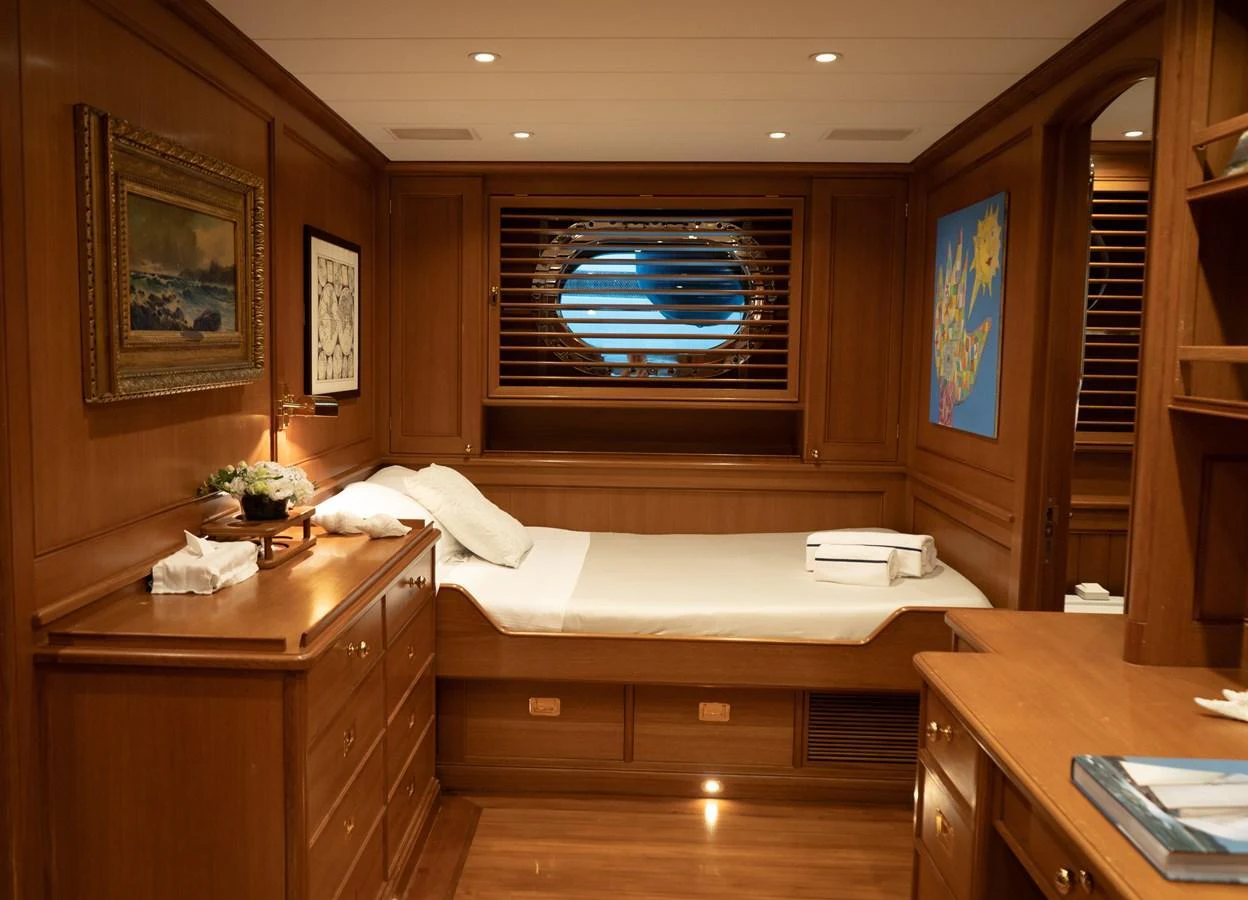 A cozy and elegant stateroom with wooden furnishings and a large porthole window. aboard HERITAGE M Yacht for Sale