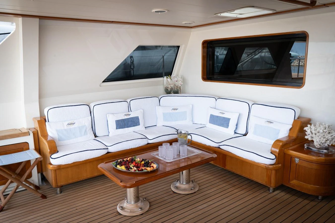 The aft deck features a cozy seating area with plush cushions and a wooden table set for refreshments. aboard HERITAGE M Yacht for Sale