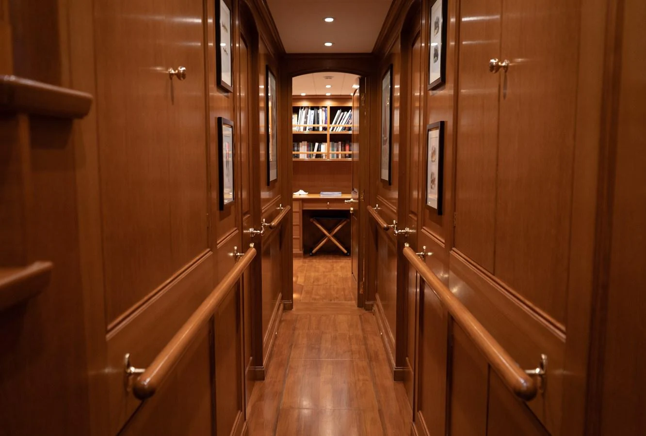 A warm, wood-paneled hallway leads to a cozy study area with bookshelves. aboard HERITAGE M Yacht for Sale