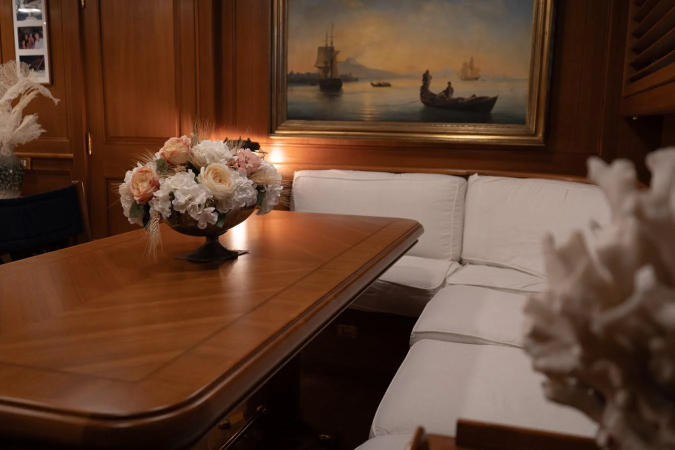 A cozy dining area with a wooden table, white cushioned seating, and a maritime painting on the wall. aboard HERITAGE M Yacht for Sale