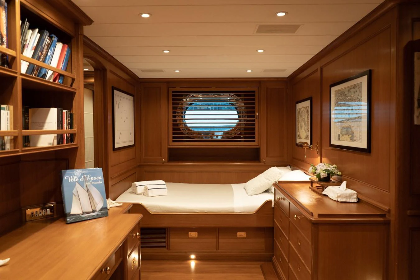 A cozy stateroom with wooden furnishings and a single bed, featuring a porthole window and ample storage space. aboard HERITAGE M Yacht for Sale