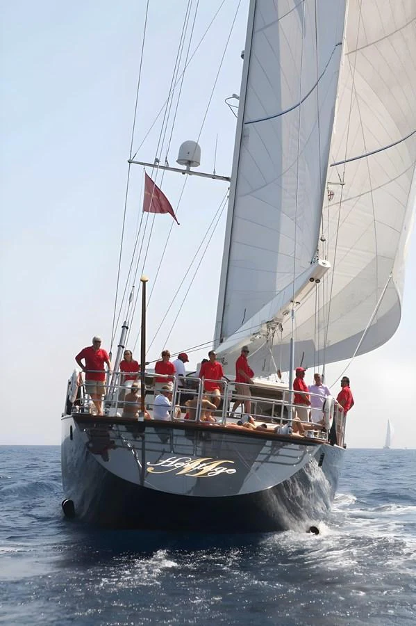 A sleek sailing yacht with crew members in red shirts navigating the open sea. aboard HERITAGE M Yacht for Sale