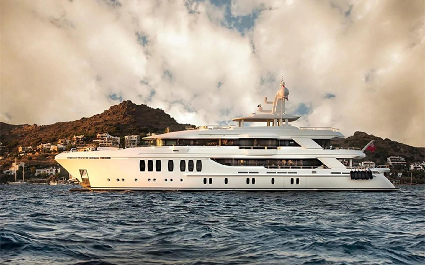 A luxurious yacht is anchored near a scenic coastline under a partly cloudy sky. aboard CMB  108 Yacht for Sale