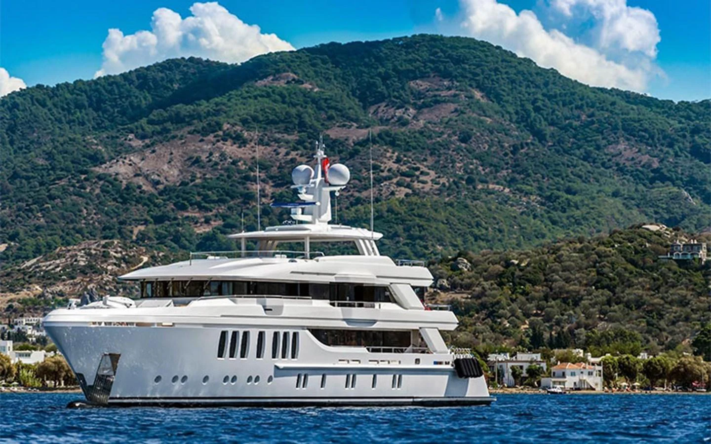 A luxurious yacht cruises along a scenic coastline with lush green hills in the background. aboard CMB  108 Yacht for Sale