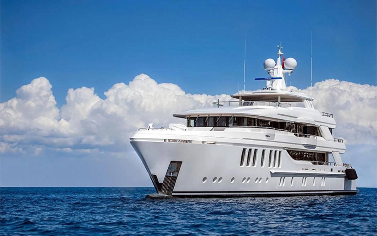 A luxurious yacht cruising on calm blue waters under a bright sky with fluffy clouds. aboard CMB  108 Yacht for Sale