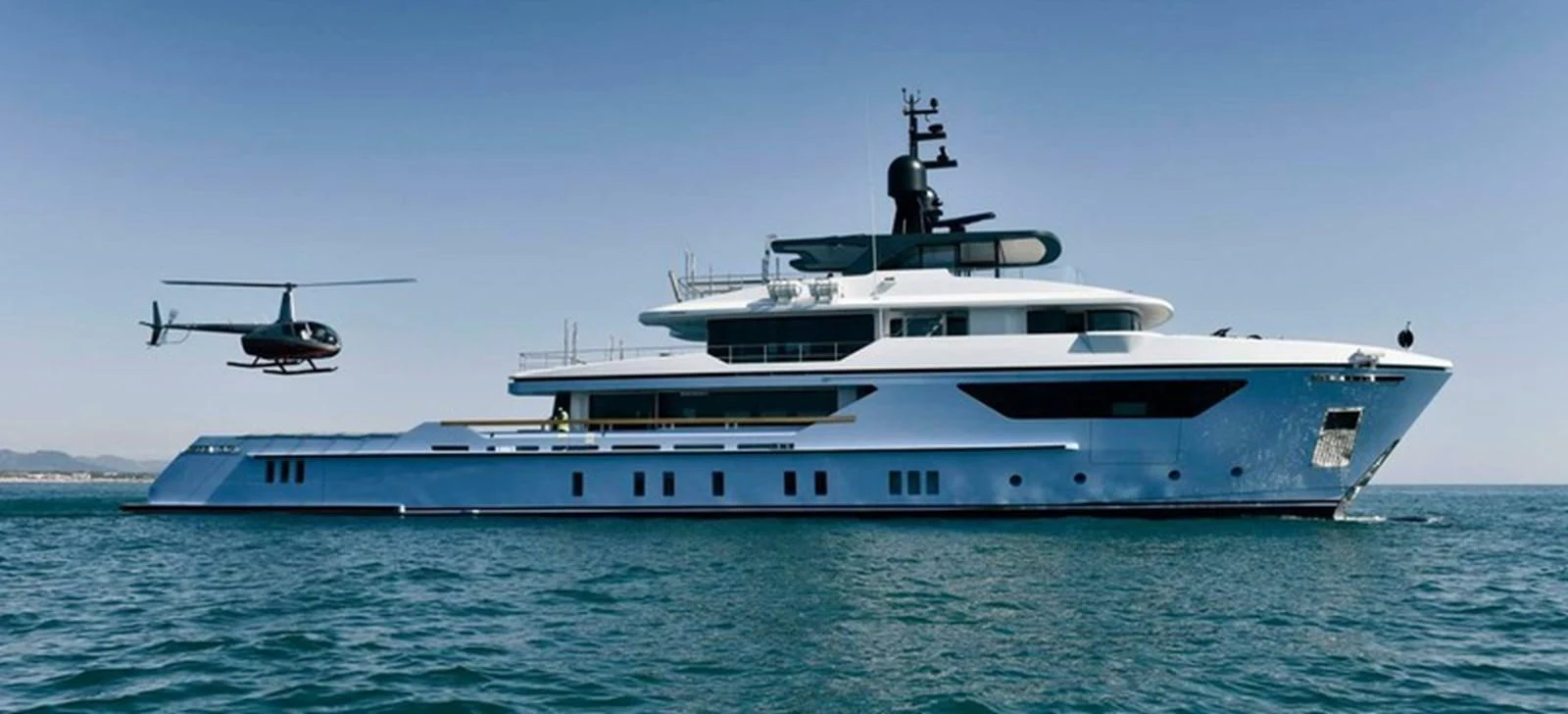A sleek, modern yacht cruising on calm waters with a helicopter hovering nearby. aboard OCEAN DREAMWALKER III Yacht for Sale