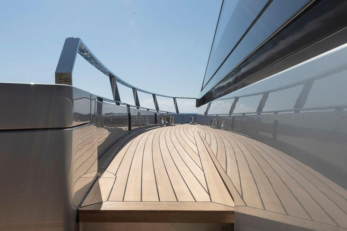 A sleek, modern yacht deck with polished railings and wooden flooring, reflecting the clear blue sky. aboard CARAT Yacht for Sale
