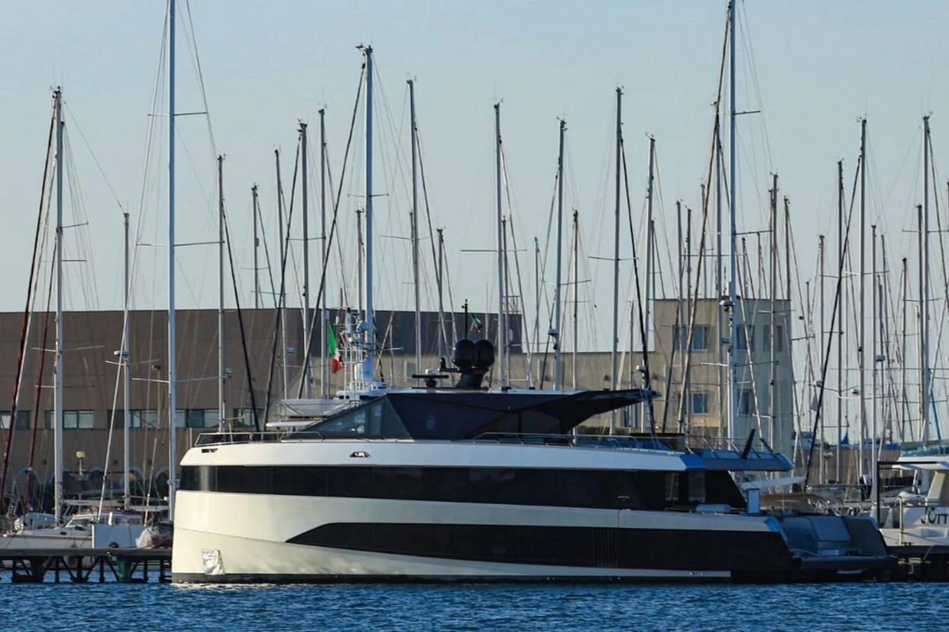 A sleek, modern yacht is docked in a marina, surrounded by numerous sailboats. aboard CARAT Yacht for Sale