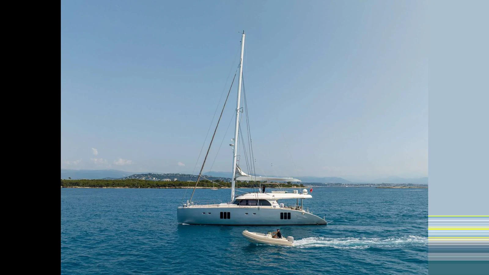 A sleek sailing yacht glides gracefully on calm blue waters, accompanied by a small tender. aboard SEAZEN II Yacht for Sale