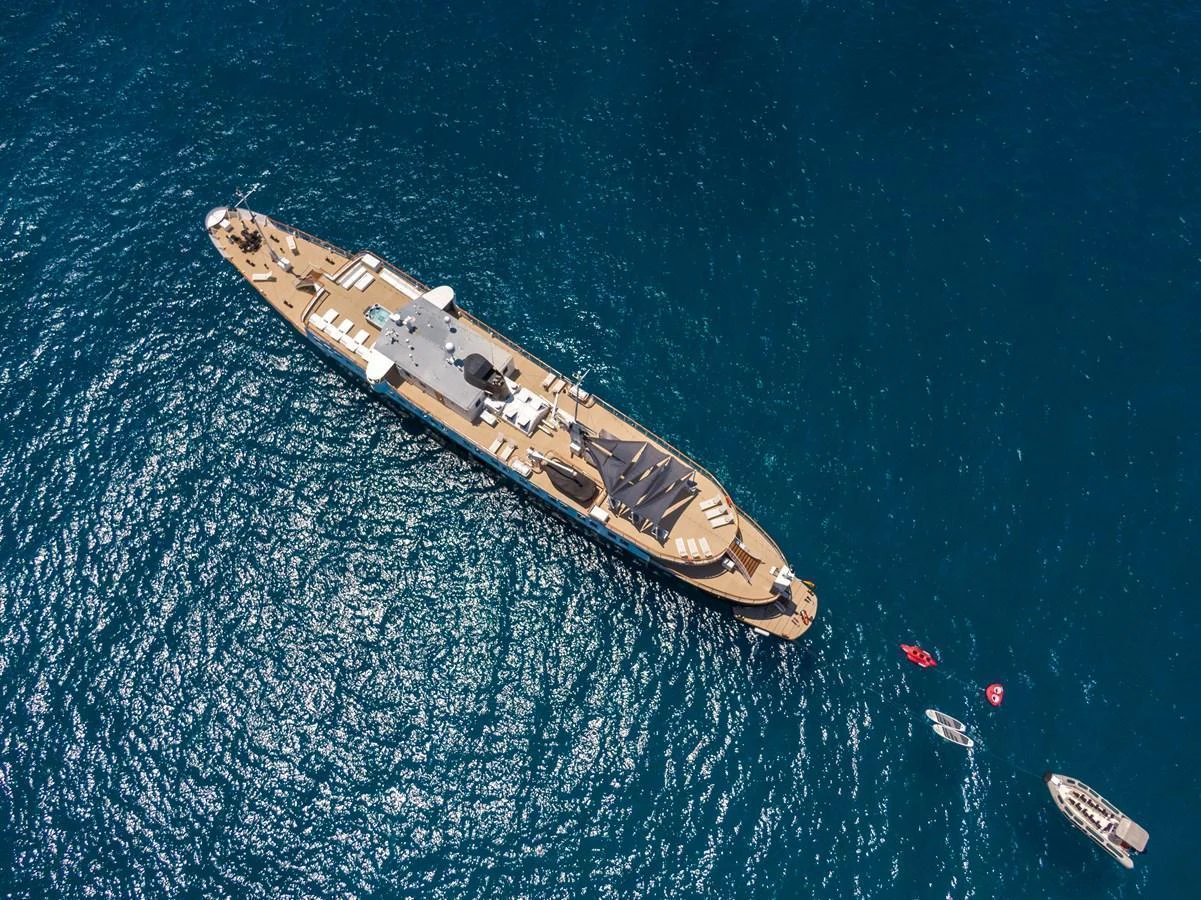 A stunning aerial view of a luxurious yacht cruising on the open sea, accompanied by smaller boats and water toys. aboard HARMONY II Yacht for Sale