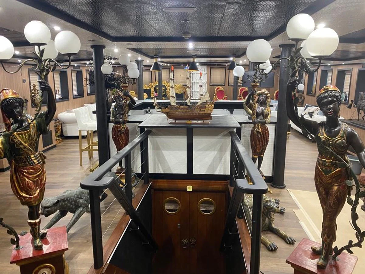 The yacht's interior features an opulent and eclectic decor with intricate statues and a model ship centerpiece. aboard HARMONY II Yacht for Sale