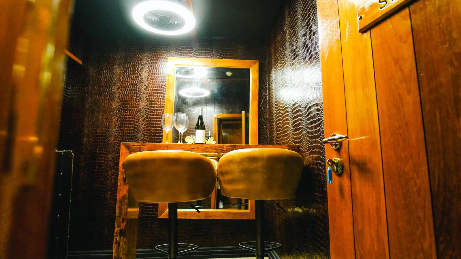 A cozy bar area with two stools and a mirror, featuring warm wooden tones and ambient lighting. aboard HARMONY II Yacht for Sale