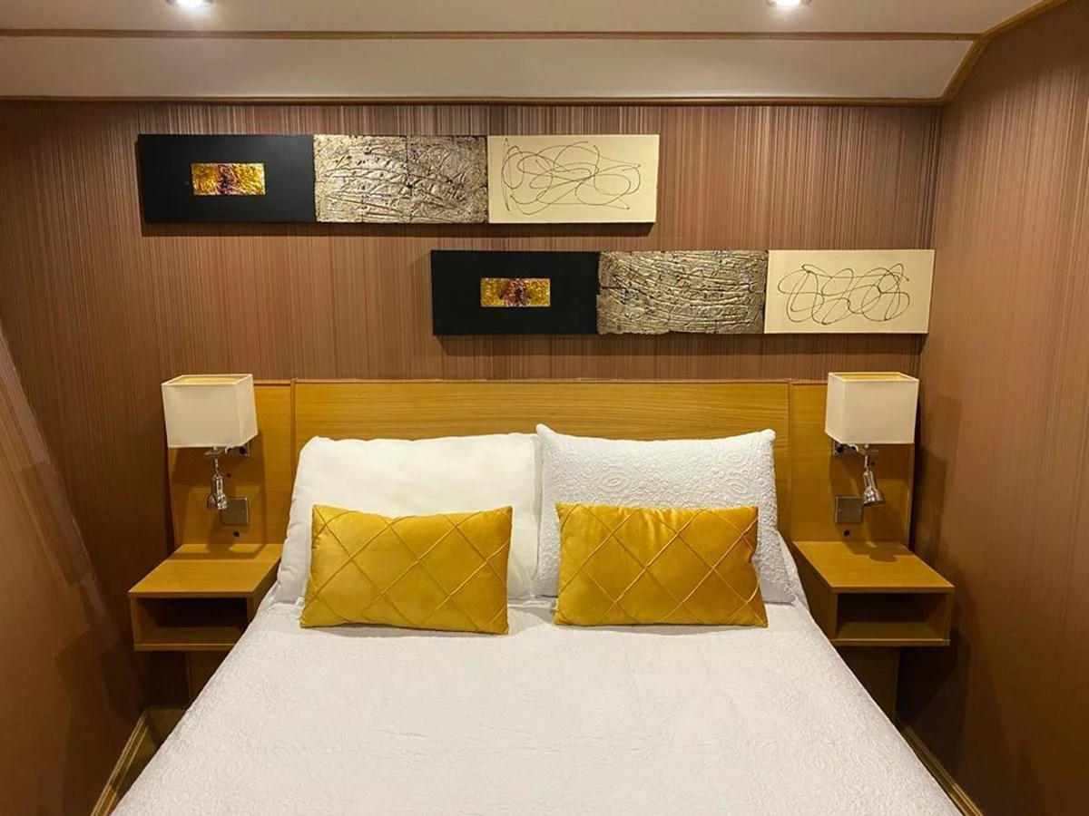A cozy stateroom with a double bed adorned with yellow accent pillows and modern wall art. aboard HARMONY II Yacht for Sale