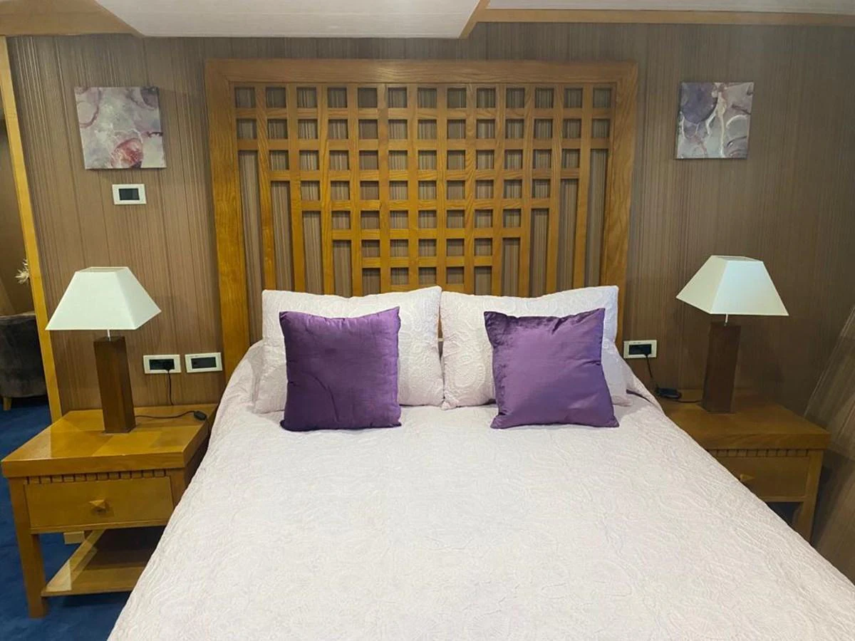 A cozy stateroom featuring a comfortable bed with purple accents and wooden furnishings. aboard HARMONY II Yacht for Sale