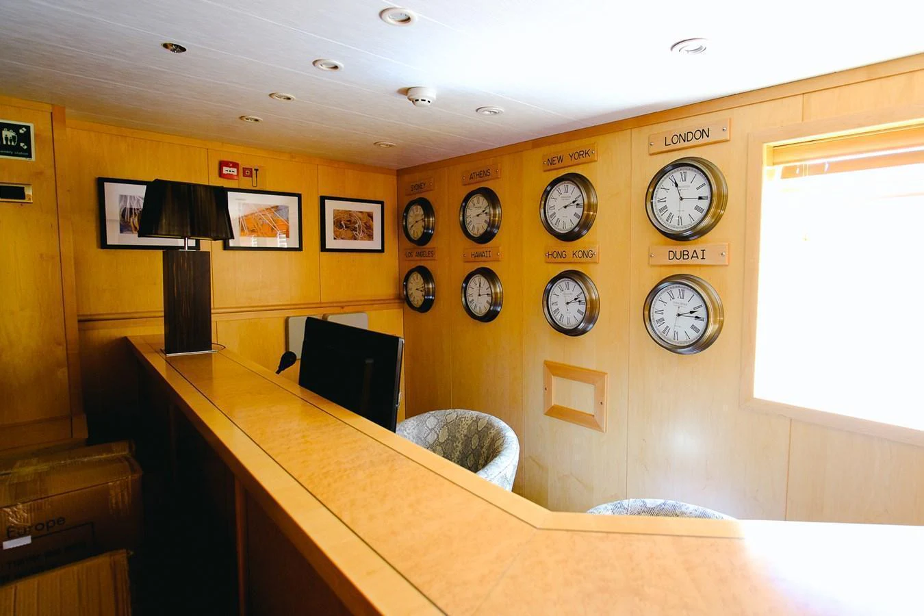 The yacht's interior features a reception area with multiple world clocks and a wooden counter. aboard HARMONY II Yacht for Sale