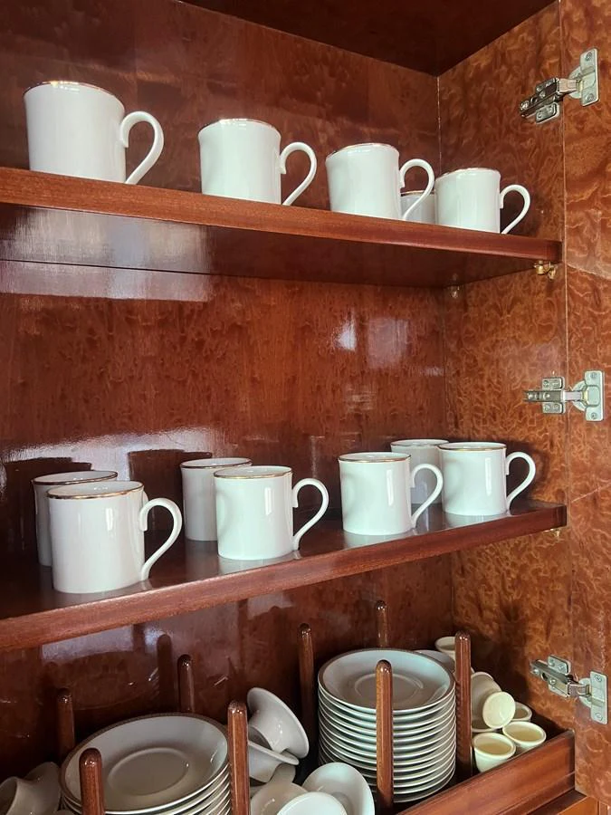 A neatly organized cabinet in the yacht's galley holds white mugs and plates. aboard HORIZON ELEGANCE 82 S Yacht for Sale