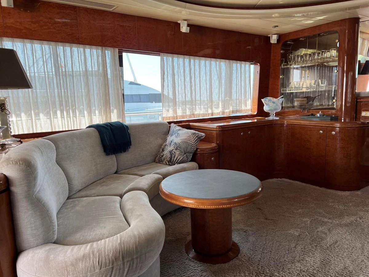 The yacht's salon features a plush curved sofa, a round wooden table, and a built-in cabinet with glassware. aboard HORIZON ELEGANCE 82 S Yacht for Sale