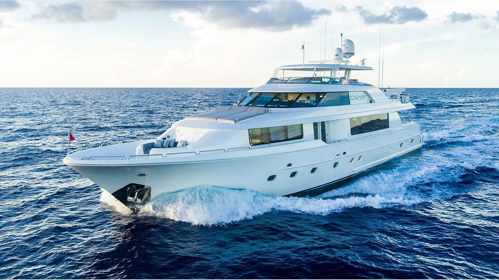 A sleek and modern yacht cruising on open water under a partly cloudy sky. aboard KEMOSABE Yacht for Sale