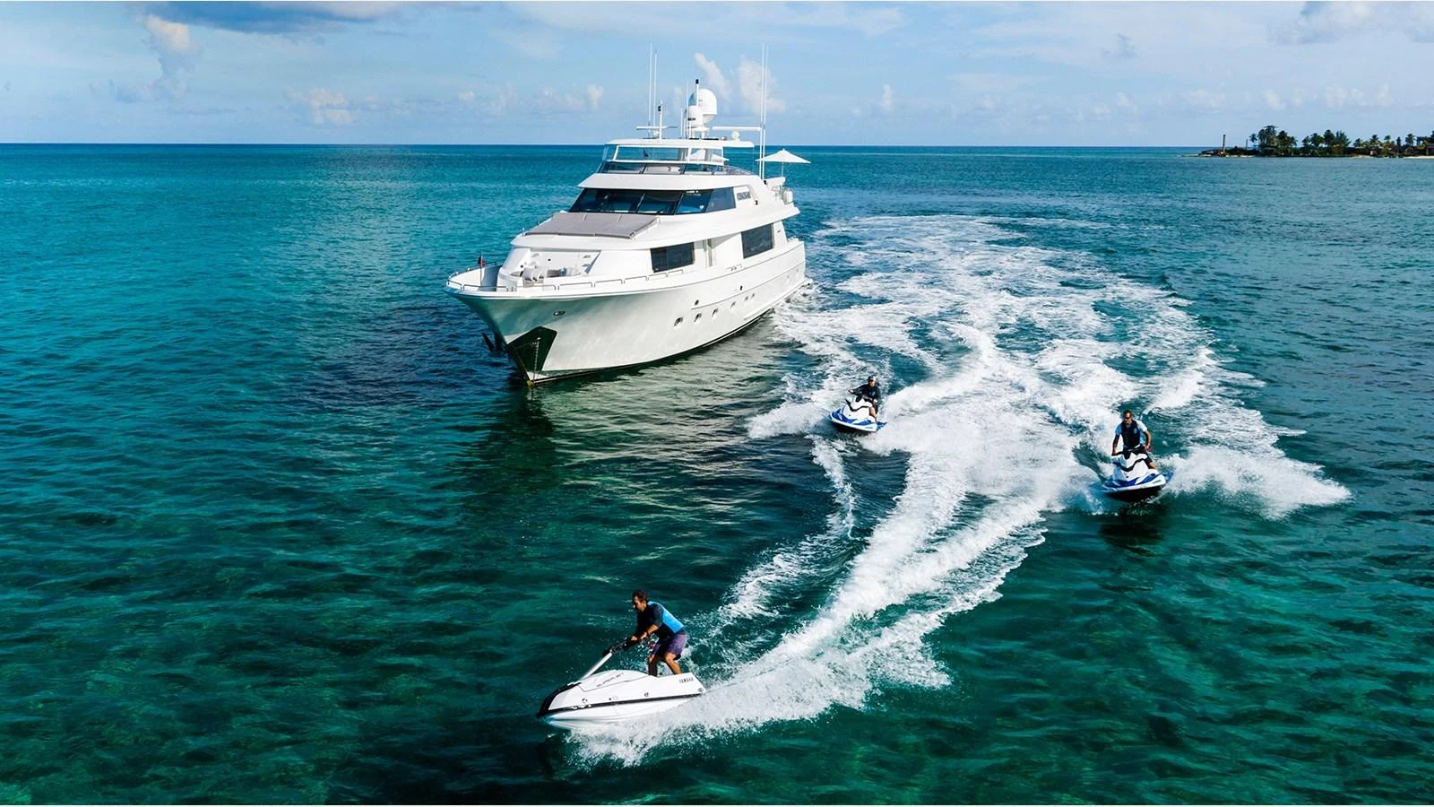 A luxurious yacht cruises through clear turquoise waters, accompanied by several jet skis. aboard KEMOSABE Yacht for Sale