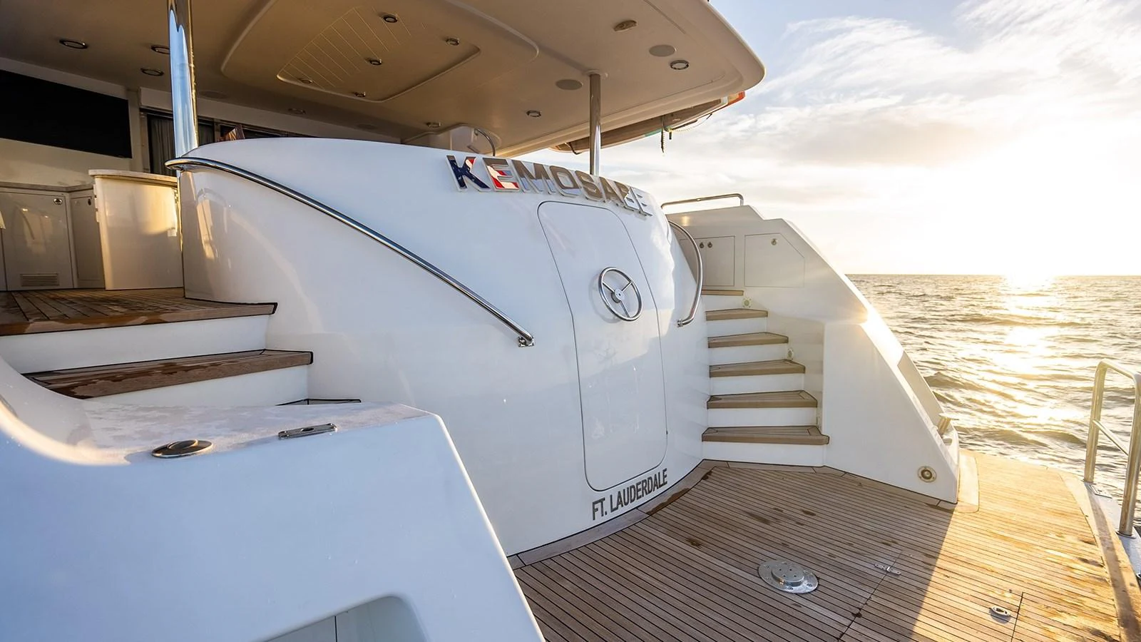 The yacht's aft deck features a spacious area with steps leading to the upper deck, bathed in golden sunlight. aboard KEMOSABE Yacht for Sale