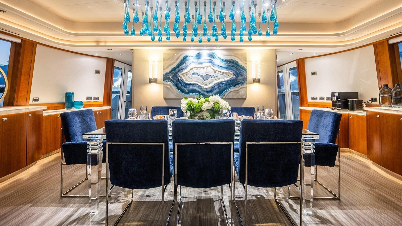 The yacht's dining area features a luxurious setting with elegant blue chairs and a stunning chandelier. aboard KEMOSABE Yacht for Sale